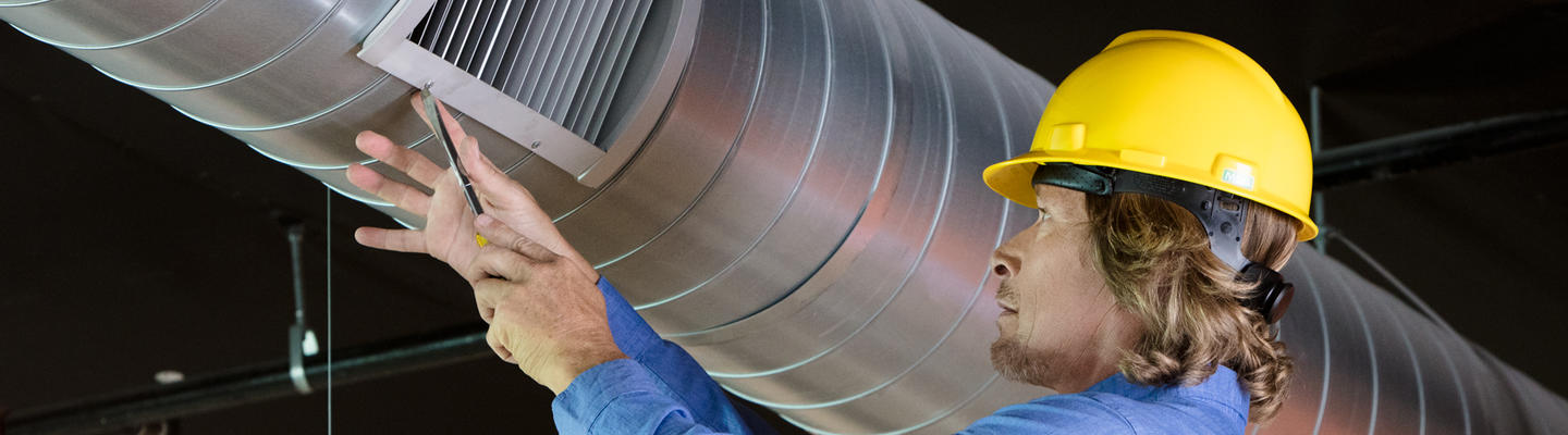 Man with yellow hardhat working on an air vent